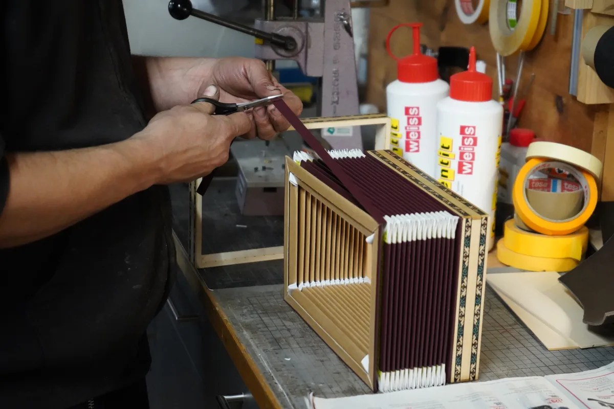 Es sind die Hände von Sergio Theiler zu sehen, wie sie an einem Balg arbeiten, der vor ihm auf einem Tisch liegt.